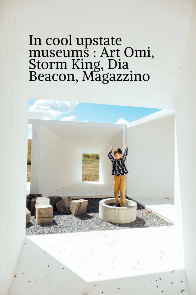 A child in a striped shirt and mustard pants stands with arms raised inside a minimalist, open-structure art installation. Perfect for 2025 photograph session ideas, this scene captures the creativity celebrated at upstate museums like Art Omi and Storm King.