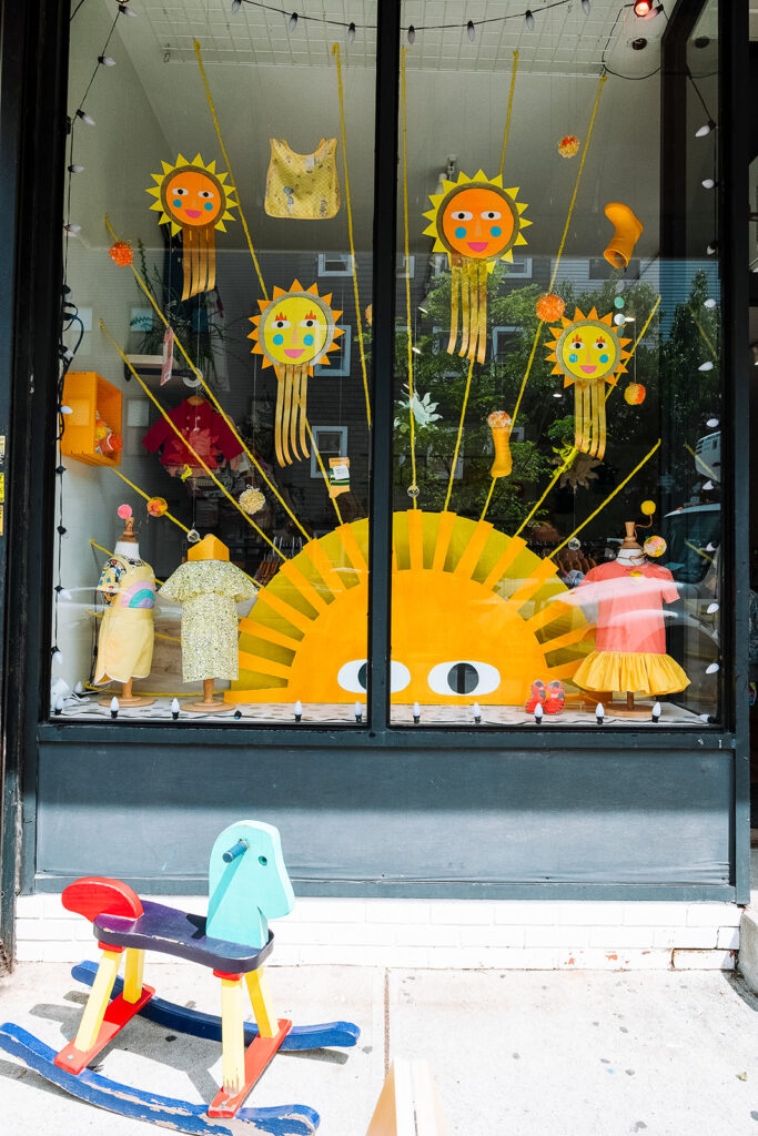 Parachute Brooklyn kids store summer window display with handmade sun decorations colorful dresses and wooden rocking horse Greenpoint Brooklyn