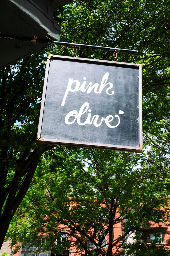 Pink Olive store hanging sign among green trees in the West Village New York City