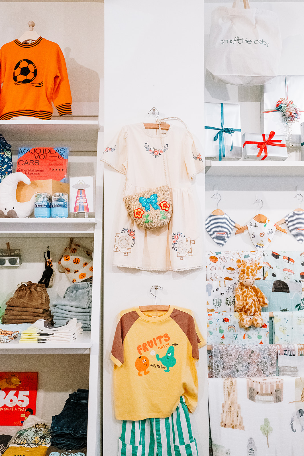 Wall display of kids clothing gift wrapped boxes and Brooklyn print bibs at Smoochie Baby Williamsburg Brooklyn